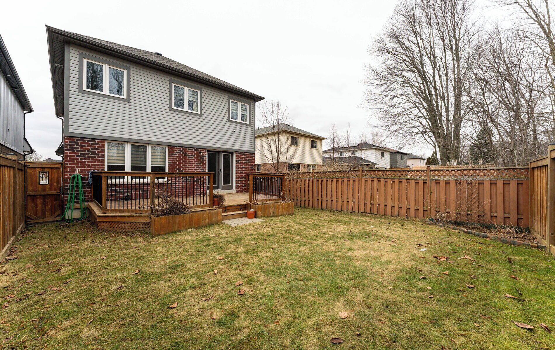 A residential backyard with a house, a wooden deck, a brick wall, and a wooden fence.
