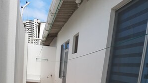 A narrow corridor with a tiled floor, white walls, and a window with blinds.