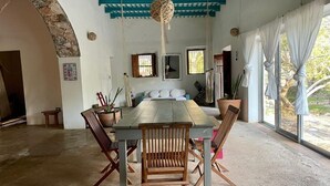 A dining area with a wooden table and chairs, a hanging light fixture, and a view of the outdoors through large windows. - Cuch Balam Private Estate with 3 Bedrooms, 2 Hectares of Garden, Pool and Cenote (Chunkanán)