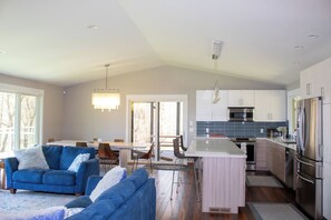 Eine moderne Küche mit Edelstahlgeräten, ein Essbereich mit Tisch und Stühlen sowie ein Wohnzimmer mit blauem Sofa.