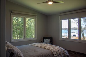 Ein Schlafzimmer mit einem Bett, zwei Fenstern, einem Sessel und einem Deckenventilator.