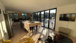A modern kitchen with a dining area, large windows, and a TV mounted on the wall. - Mollusk Alaska Retreat, Private Coastal Escape in Homer, AK (Homer)