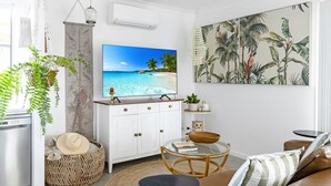 Een woonkamer met een televisie, een bank, een salontafel en een schilderij van tropische planten.