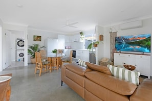 A modern living room with a leather sofa, dining area, kitchen, and a large TV.