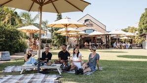 Een groep mensen zit op een deken onder parasols bij een restaurant met terras.