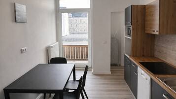 Une cuisine moderne avec un plan de travail en bois, une table à manger noire avec des chaises, et une vue sur un immeuble par la fenêtre.