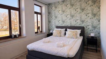A bedroom with a large bed, two bedside tables, a window with a view, and a floral wallpaper.