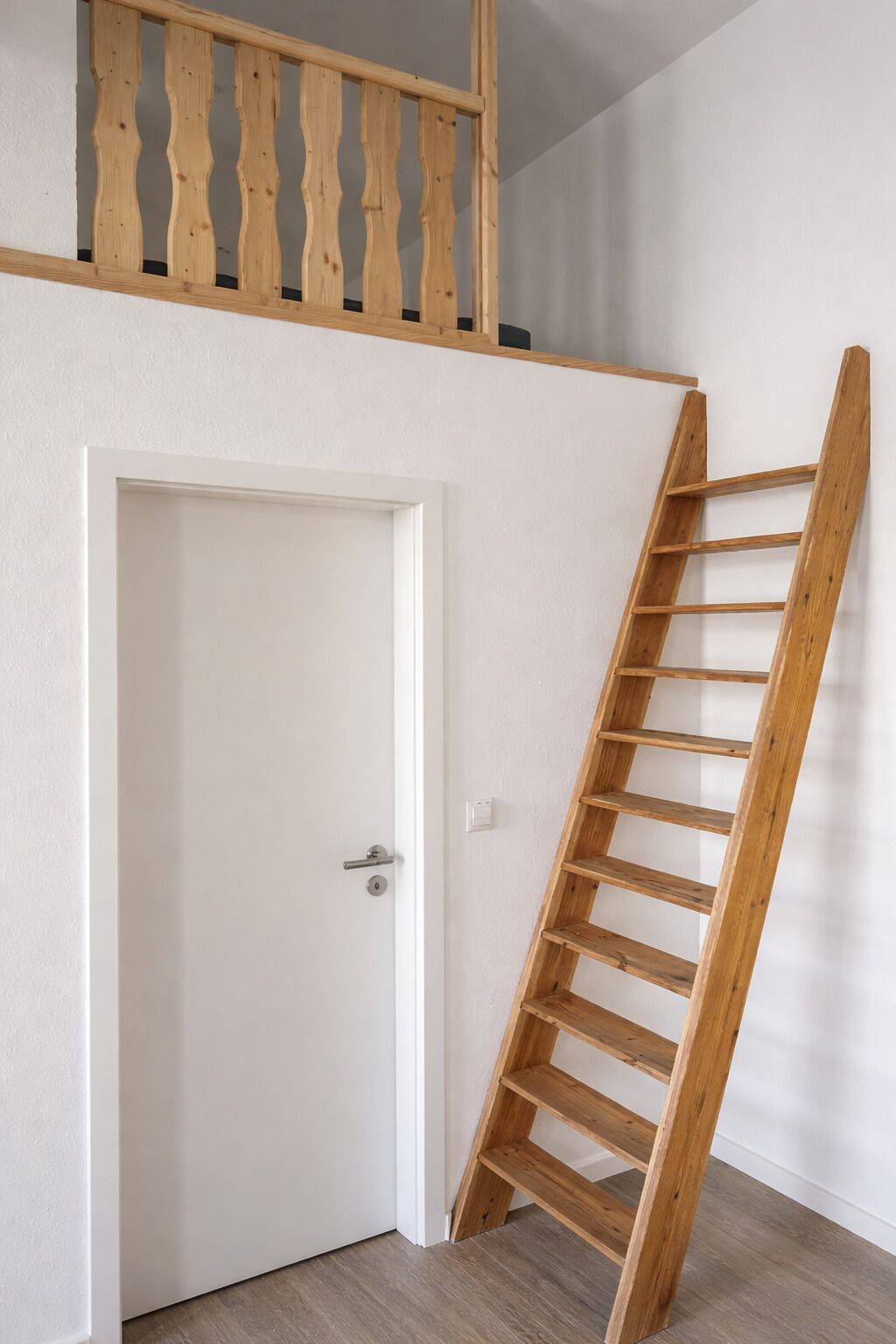 Une pièce avec une porte blanche, une échelle en bois et un mur blanc.