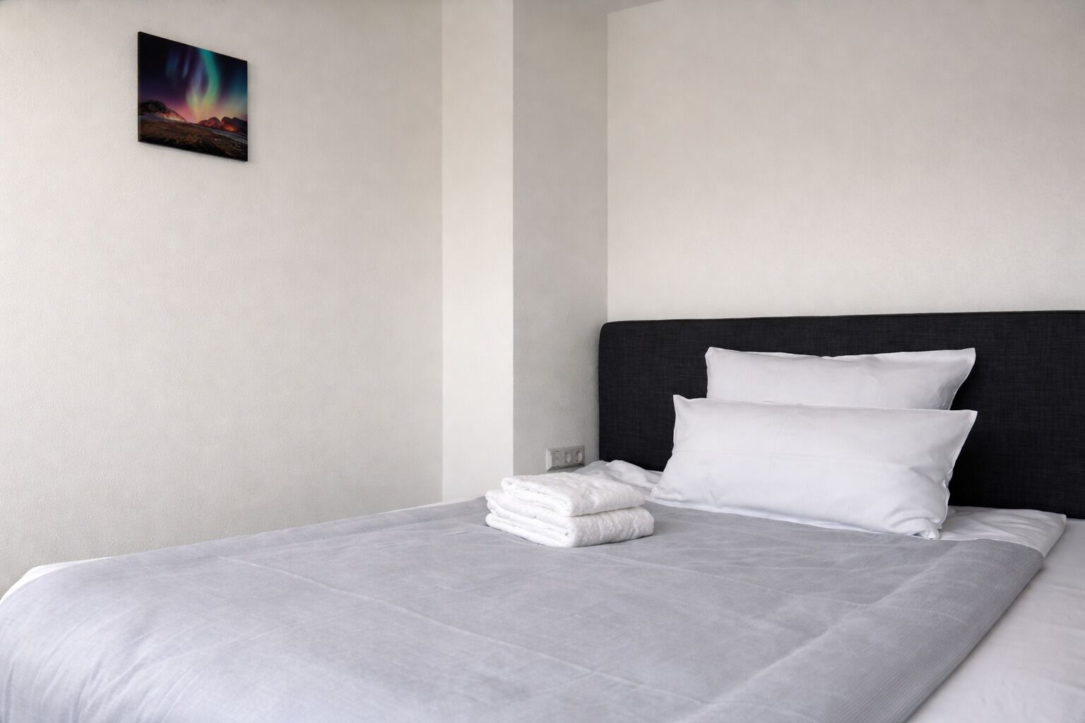 A neatly made bed with white linens, a dark headboard, and a single artwork on the wall.