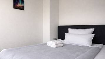 A neatly made bed with white linens, a dark headboard, and a single artwork on the wall.