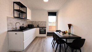 A compact kitchen with a sink, stove, and a dining area with chairs and a table. - MIILOX Apartments Chemnitz (Chemnitz)