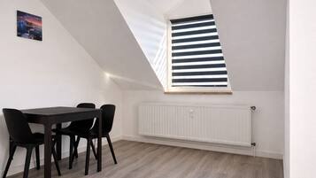 Ein Zimmer mit schrägen Wänden, einem Oberlicht, einem Esstisch mit Stühlen und einer Heizung.