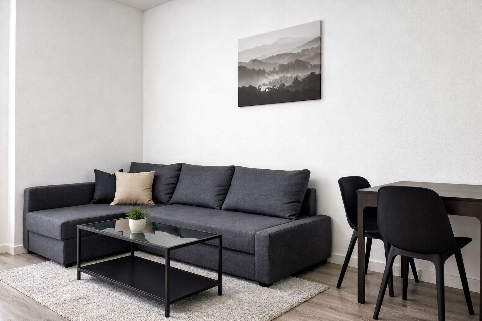 Un salon moderne avec un canapé gris, une table basse, une table à manger avec des chaises et un tableau encadré au mur.