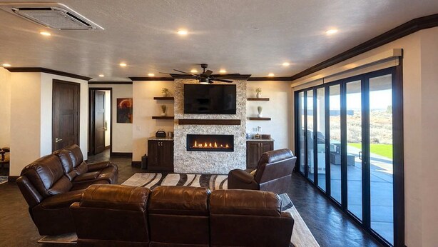 A modern living room with a fireplace, leather sofas, a flat-screen TV, and a large window offering a view of the outdoors. - Spacious Modern Home Near Zion & Grand Canyon (Colorado City)