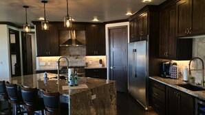 A modern kitchen with dark wood cabinets, stainless steel appliances, and a central island with bar stools. - Spacious Modern Home Near Zion & Grand Canyon (Colorado City)