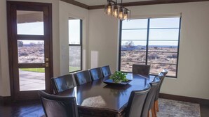 A dining room with a large table, chairs, a chandelier, and a view through a window. - Spacious Modern Home Near Zion & Grand Canyon (Colorado City)