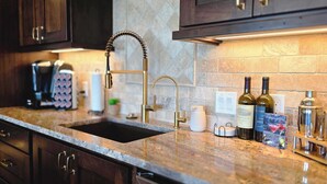 A kitchen with dark wooden cabinets, a granite countertop, a gold faucet, and a wine bottle. - Spacious Modern Home Near Zion & Grand Canyon (Colorado City)