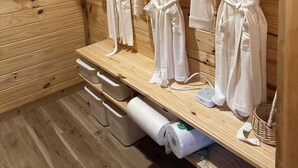 Un sauna de madera con batas blancas colgadas en colgadores, un banco de madera y un dispensador de toallas.