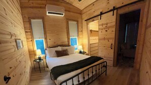 Un dormitorio de cabaña de madera con cama, lámparas de noche, ventilador de techo y una puerta que da al exterior.