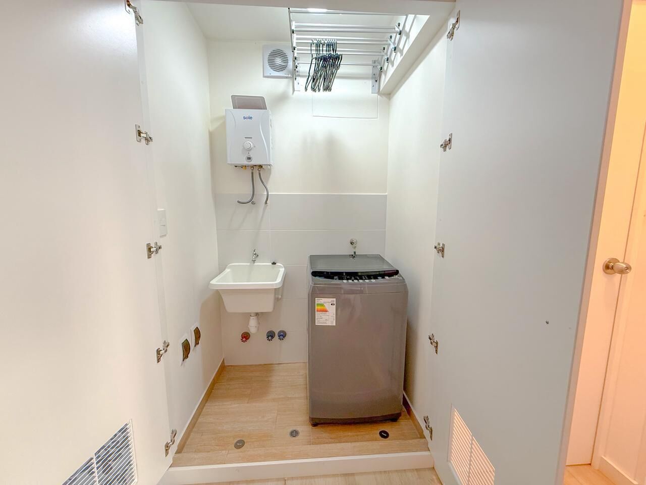 Een kleine badkamer met een wastafel, een boiler en een compacte wasmachine.