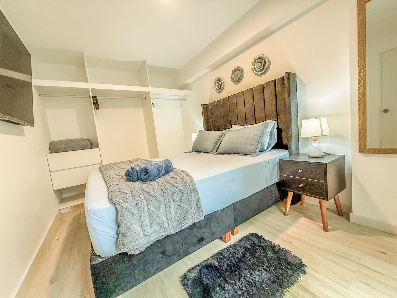 Un dormitorio con cama, mesita de noche, lámpara y espejo en la pared.