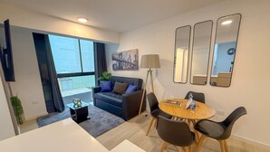 Ein modernes Wohnzimmer mit einer Couch, einem Esstisch mit Stühlen, einer Stehlampe und einem großen Fenster.