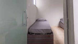 A small, narrow room with a single bed, a window, and a door. - Apartamento Para 6 h Spedes com Wi-fi e Garagem (Para de Minas)