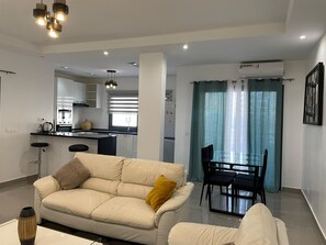 Un salon moderne avec un canapé, une table à manger et des chaises, et une cuisine en arrière-plan.