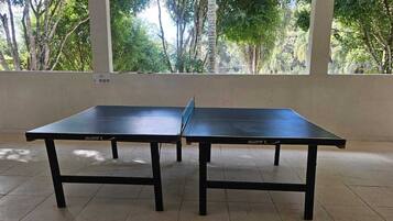 Uma mesa de pingue-pongue em um ambiente com piso ladrilhado e grandes janelas.