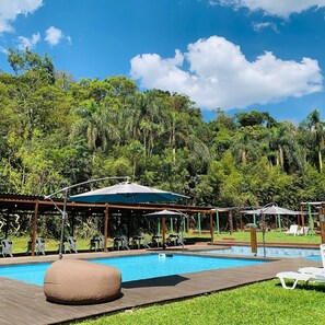 Zona de piscina amb gandules i ombrelles, envoltada de vegetació abundant.