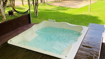 Un jacuzzi bajo una carpa, con un patio cubierto de césped y árboles al fondo.