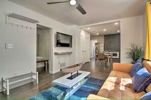 Un salon moderne avec un canapé, une table basse, un téléviseur et, au fond, un coin repas.