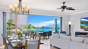 A dining area with a view of the ocean, a living room with a sofa and TV, and a ceiling fan. - Honua Kai | Ocean View 8 BR, Sleeps 22 | Car Incl. w/ 6+ Nights | HKH ML-2618 by KBM (Lahaina)