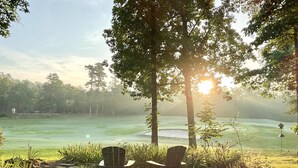 A stone pathway leading to two Adirondack chairs overlooking a golf course with a misty background and a sunlit sky. - Birdie House on Balboa (Hot Springs Village)