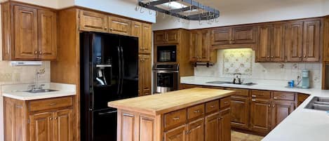 Una cocina con armarios de madera, un refrigerador negro, una isla central y tragaluces.