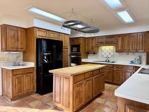A kitchen with wooden cabinets, a black refrigerator, a central island, and skylights. - Birdie House on Balboa (Hot Springs Village)