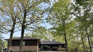 A single-story house with a brick exterior, a covered front porch, and a gravel driveway. - Birdie House on Balboa (Hot Springs Village)