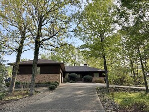 A single-story house with a brick exterior, a covered front porch, and a gravel driveway. - Birdie House on Balboa (Hot Springs Village)