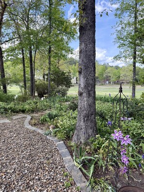 A garden with a gravel path, trees, and purple flowers. - Birdie House on Balboa (Hot Springs Village)