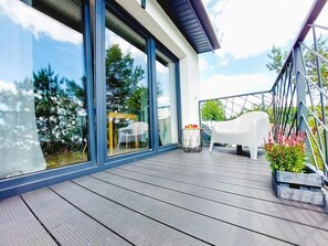 A modern outdoor deck with a glass door leading to a patio area, a white chair, and a small table with flowers. - mrhomeapartments-Limba (Kraków)