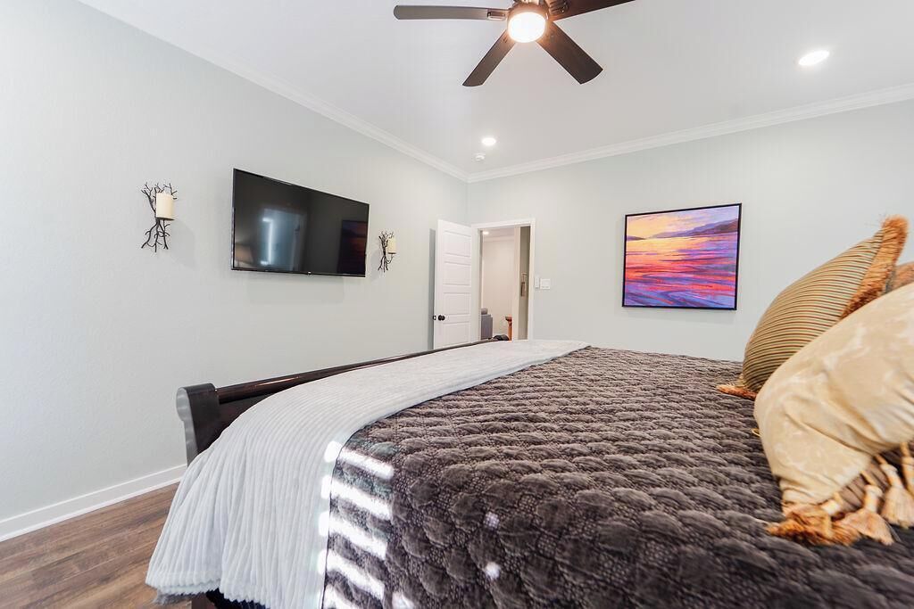 A bedroom with a bed, a ceiling fan, a TV, and a door leading to another room.