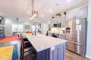 A modern kitchen with stainless steel appliances, a marble island, and a dining area with wooden chairs. - Newer Build 2024 Home near Granada Golf Course (Hot Springs Village)
