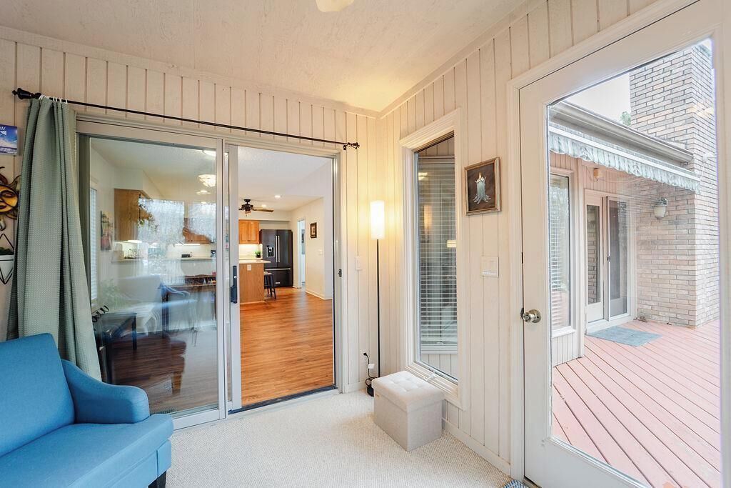 A room with a sliding glass door leading to a kitchen, a blue sofa, and a small white bench.