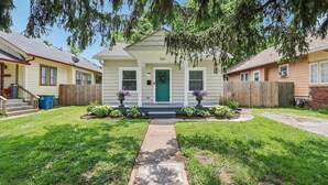 Une maison à deux étages avec une porte verte, un porche à l’avant et un chemin menant à l’entrée.