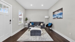 Un salon moderne avec un canapé gris, une table basse, un pouf gris, une lampe sur pied et un tableau représentant une scène de plage.
