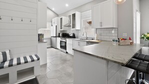 Une cuisine moderne avec des meubles blancs, un îlot central et un coin repas agrémenté d’un banc.