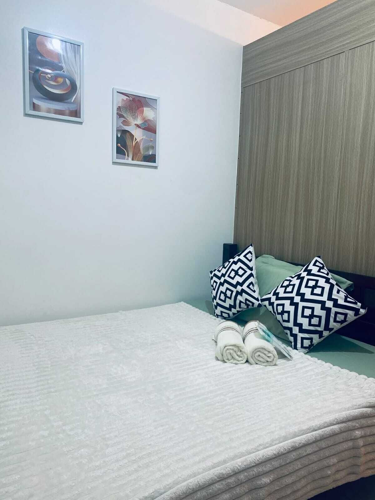 A neatly made bed with patterned pillows, a headboard, and two framed artworks on the wall.