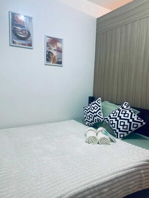 A neatly made bed with patterned pillows, a headboard, and two framed artworks on the wall. - J&C Staycation (Pasay)