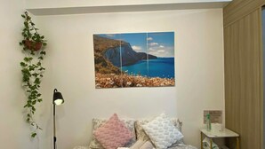 Ein Schlafzimmer mit einem Bett, einem Wandbild, einem Nachttisch und einer hängenden Pflanze.