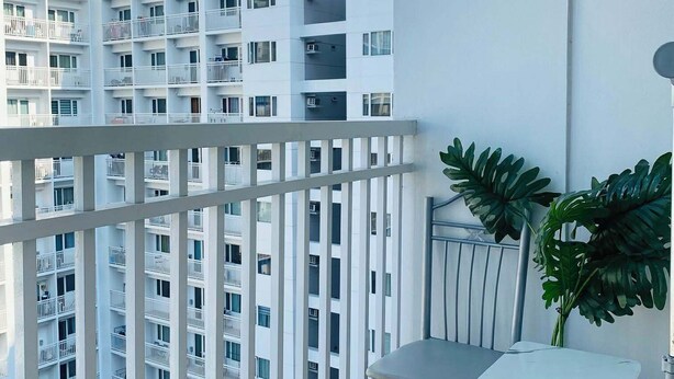 Ein Balkon mit weißer Brüstung, einem kleinen Tisch, einem Stuhl und einem Blumentopf.